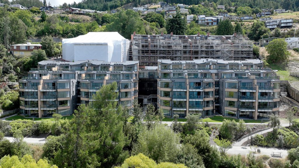 Oaks shore hotel and apartment remediation, showing completed stage 1 and 2, stage 3 under shrinkwrap, and stage 4 with scaffolding. Queenstown, New Zealand