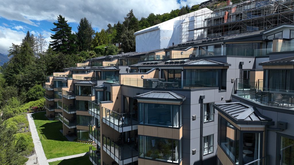 Oaks shore hotel and apartment remediation, showing completed stage 1 and 2, stage 3 under shrinkwrap, and stage 4 with scaffolding. Queenstown, New Zealand